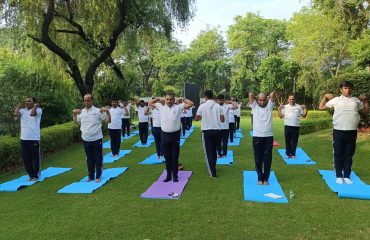 RCI officials performing yoga outdoors on Yoga Day, standing on mats with arms bent at elbows