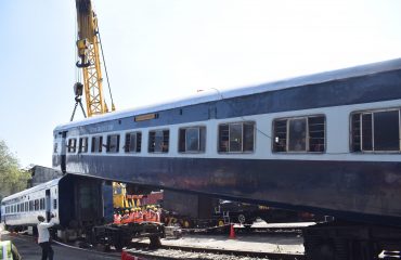 आपत्कालीन सामान्यीकरणाच्या प्रयत्नांचा भाग म्हणून क्रेनने रुळावरून घसरलेला रेल्वे डबा उचलला जात आहे