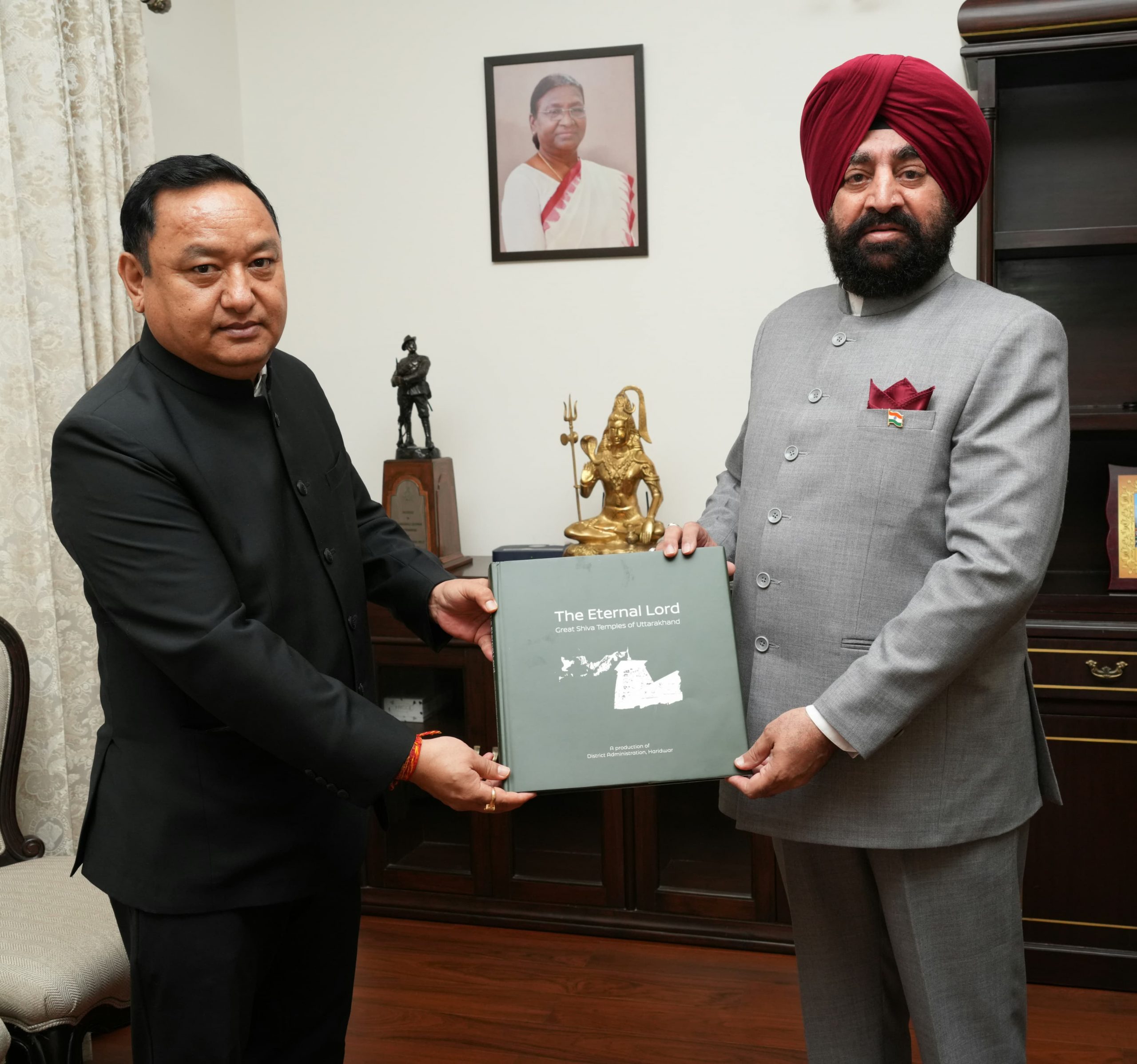 Dhiraj Singh Garbyal, DM Haridwar pays a courtesy visit on the Governor and presents a coffee table book titled, 'The Eternal Lord-Great Shiva Temples of Uttarakhand'.