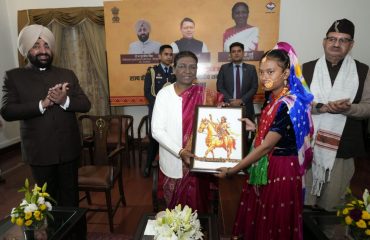 A woman from a tribal group presents a painting to President Smt. Draupadi Murmu.